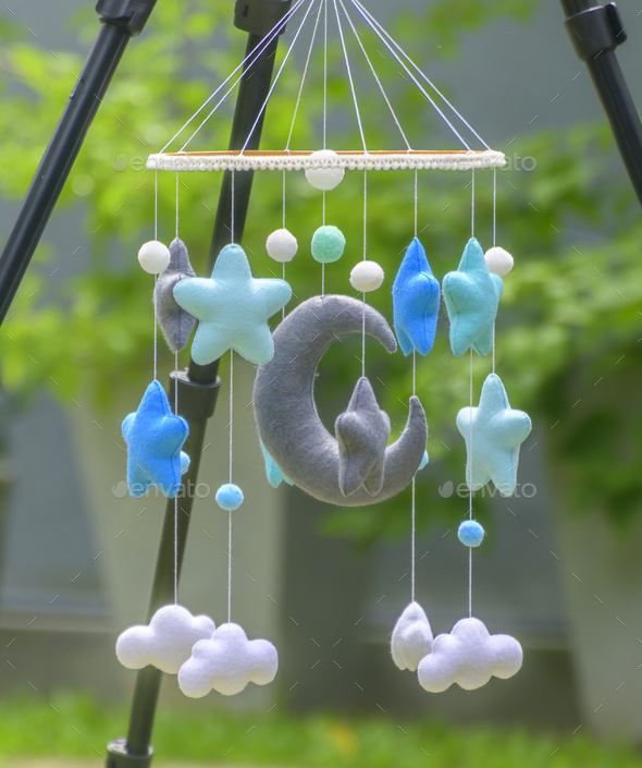 Baby cot mobile hangs from a camera tripod in the outdoor garden. Stock